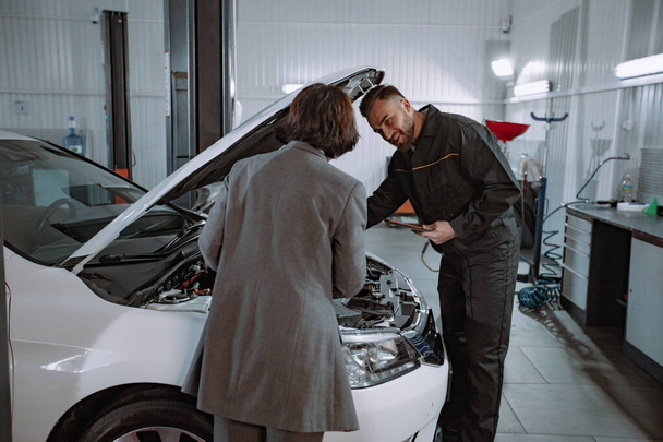 Servicio mecánico de centro automático tener una conversación con la mujer cliente que le muestra algo en el motor del coche
 - Foto, Imagen