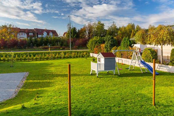 Зеленый сад с красивым деревянным домом для детей и детской площадкой осенью
. - Фото, изображение