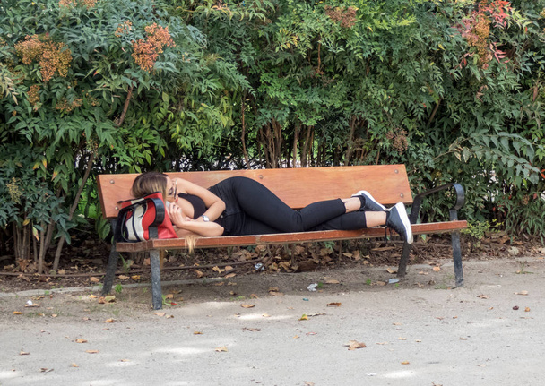 Madrid, Spain, October 7, 2019. Young girl lying on park bench in black jeans and top. - Foto, afbeelding