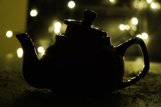 the shadow of the kettle on a dark background and light bulbs. Dark background. Vintage black ceramic teapot. - Valokuva, kuva
