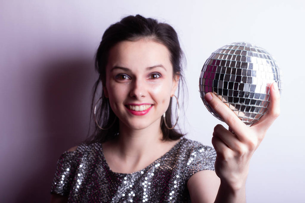 beautiful young girl in a shiny T-shirt holds a disco ball in her hands - Photo, Image