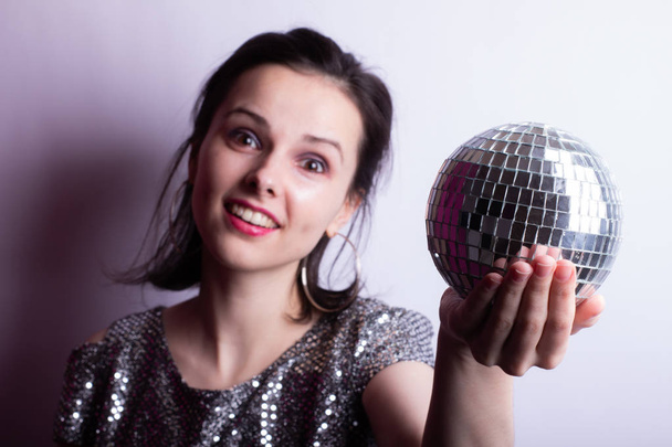 beautiful young girl in a shiny T-shirt holds a disco ball in her hands - Zdjęcie, obraz