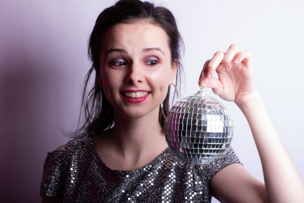 beautiful young girl in a shiny T-shirt holds a disco ball in her hands - Fotografie, Obrázek