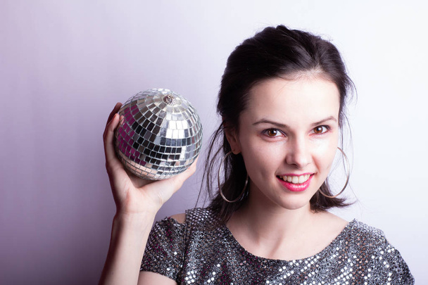 beautiful young girl in a shiny T-shirt holds a disco ball in her hands - Foto, imagen