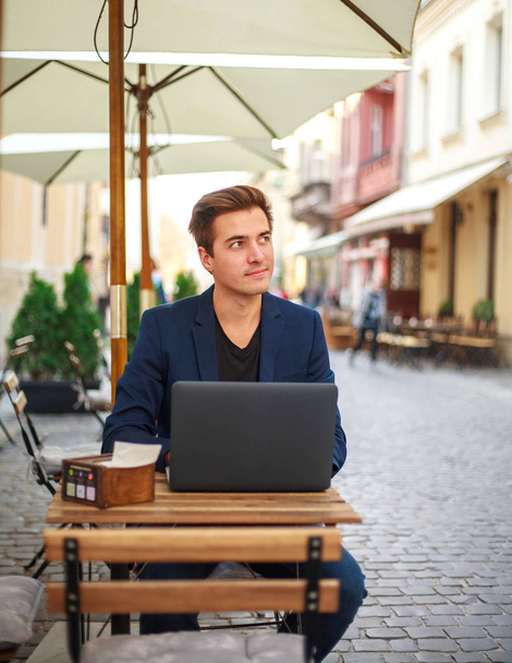 Young guy business man with laptop at table of summer cafe - Фото, изображение