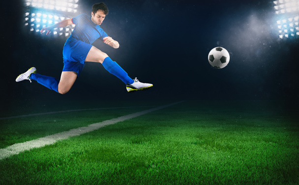 Футбольная сцена в ночном матче с футболистом, бегущим пнуть мяч на стадионе
 - Фото, изображение