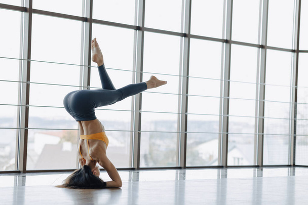 jovem menina atraente fazendo exercícios de fitness com ioga no chão contra o fundo de janelas panorâmicas
 - Foto, Imagem
