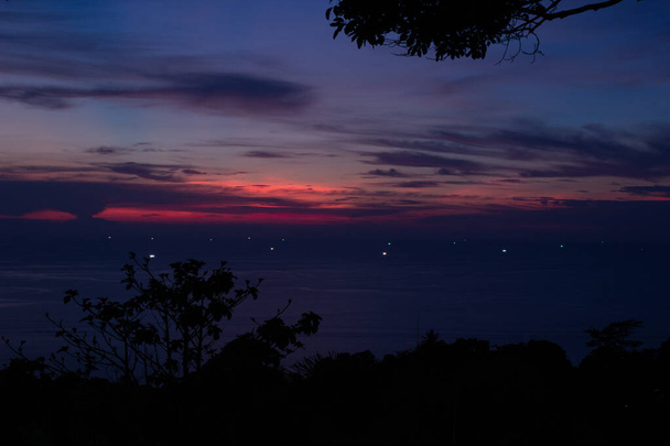 Een donkere en levendige zonsondergang gezien vanaf de top van Karon Viewpoint in Phuket Thailand. Een diepe oranje zon ondergegaan achter zware wolken boven de oceaan. - Foto, afbeelding
