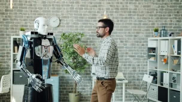 Happy developer dancing in office room with smart robot having fun at work - Metraje, vídeo