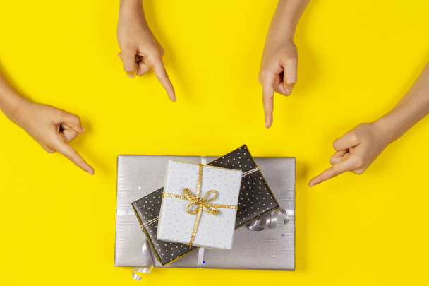 Many hands pointing to wrapped present gift boxes on yellow background. Top view - Photo, Image