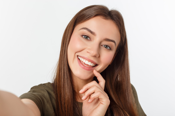 Retrato de uma mulher bonita sorrindo fazendo foto selfie no smartphone isolado em um fundo branco
. - Foto, Imagem