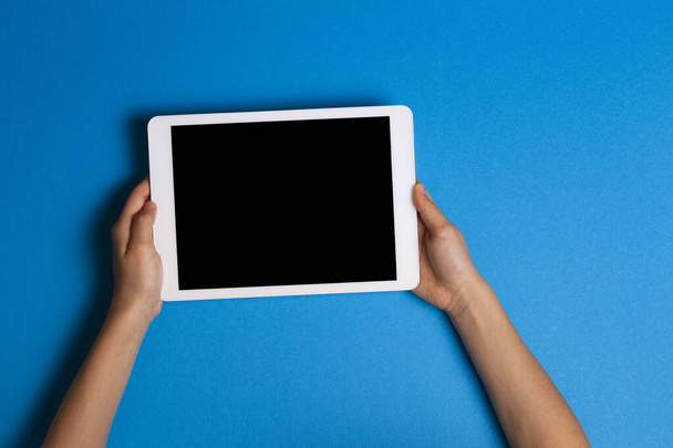 Kinderhände mit weißem Tablet-Computer auf hellblauem Hintergrund - Foto, Bild