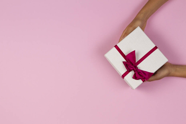 Χέρια κρατώντας δώρο παρουσιάζει κουτί πάνω από ανοιχτό ροζ φόντο. Άνω όψη - Φωτογραφία, εικόνα