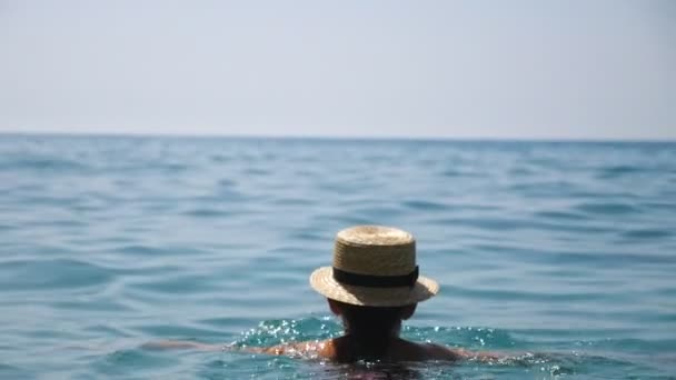 Woman in sunglasses swimming in open sea enjoying summer vacation and admiring scenic seascape. Girl relaxing on exotic resort floating in azure clear water. Concept of holiday. Back view Slow motion - Footage, Video