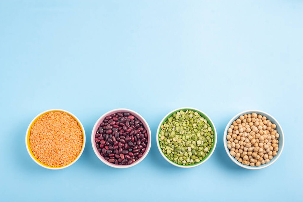 Dried beans, lentils, green horn and chickpeas in round plates on a blue background - Photo, Image