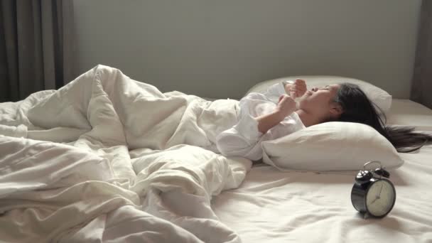 eine junge asiatische Frau blickte auf den Wecker, sie war schockiert, stand aus dem Bett auf, weil es zu spät war. - Filmmaterial, Video