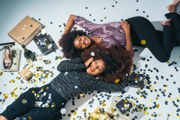 Top view of Two Happy American African Women laying on the floor celebrating new years eve with confetti, gifts and champagne. - Foto, Imagem
