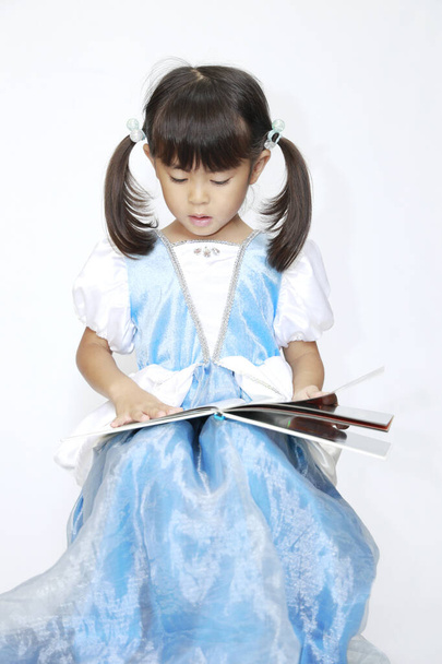 Японська дівчинка читає книжку в сукні (4 роки).) - Фото, зображення