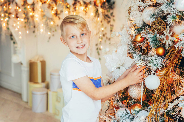 Young boy decorating Christmas tree on Christmas eve at home. Young kid in light bedroom with winter decoration. Happy family at home. Christmas New Year december time for celebration concept - 写真・画像
