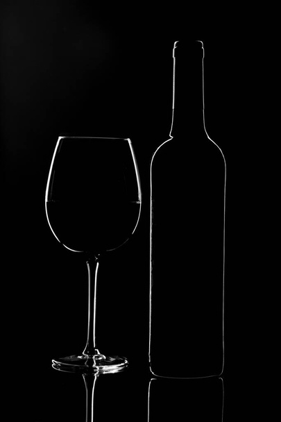 Empty wine glass and a bottle isolated on a dark background - Фото, изображение