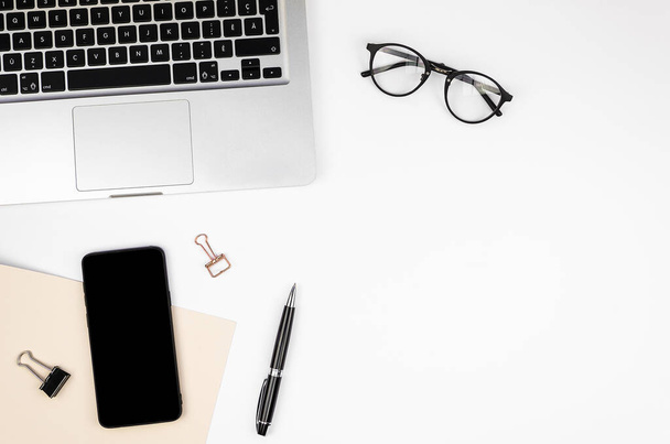 Flat lay frame mockup branco Desk com um laptop prateado, óculos, caneta e smartphone com uma tela preta. Visão superior com espaço de cópia para captura de tela ou texto. Empresa conceito de local de trabalho corporativo
 - Foto, Imagem