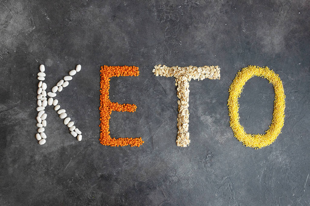 Keto word made from ketogenic food. Keto, Ketogenic diet, low carb. Healthy food concept - top view. Organic products: lentils, oatmeal, beans, millet on a dark gray background. - Photo, Image