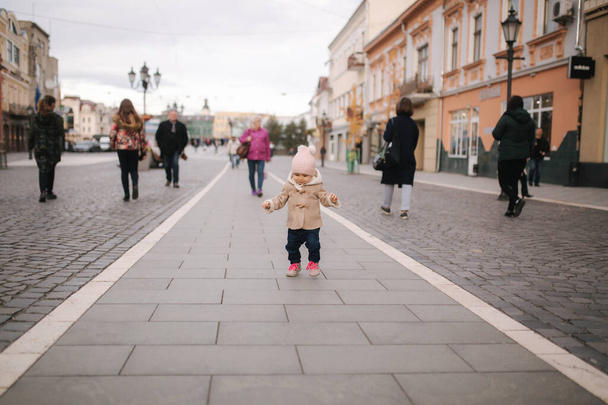Happy baby girl walking in the city in autumn time. Cute baby in brown coat and jeans - Fotó, kép