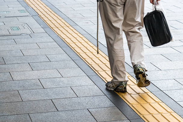 Blind αγνώριστο άτομο που περπατά σε μια απτική πλακόστρωση μονοπάτι, πίσω όψη, σε εξωτερικούς χώρους - Φωτογραφία, εικόνα