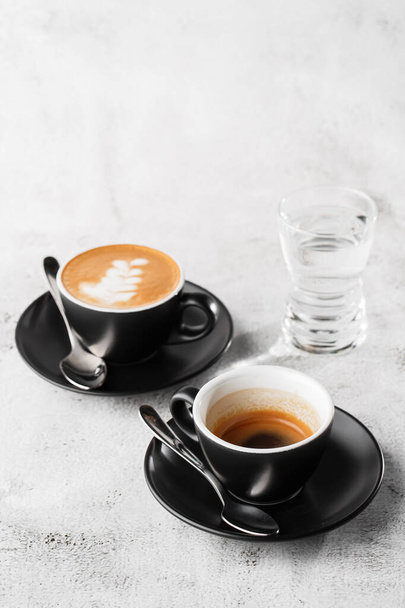 Two dark cups of hot black coffee, espresso, cappuccino with milk isolated on bright marble background. Overhead view, copy space. Advertising for cafe menu. Coffee shop menu. Vertical photo. - Photo, Image