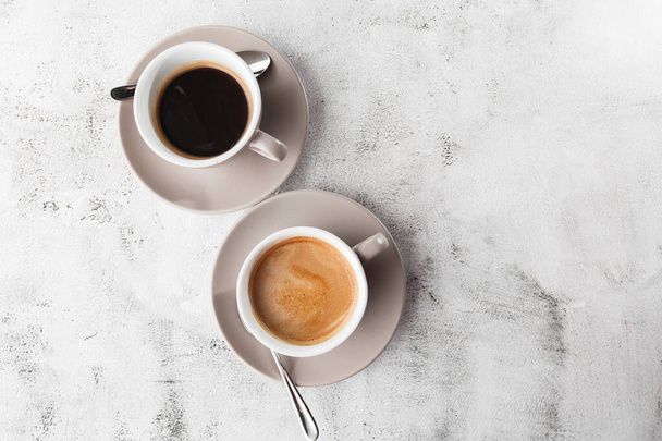 Two white cups of hot black coffee with milk isolated on bright marble background. Overhead view, copy space. Advertising for cafe menu. Coffee shop menu. Horizontal photo. - Foto, immagini