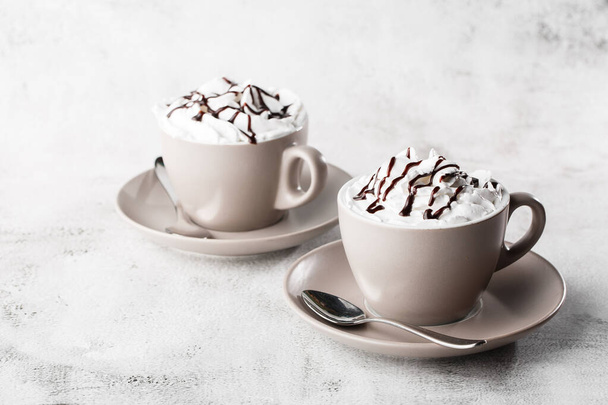 Two cups of coffee with whipped cream and chocolate topping. Iced frappuccino in white cup isolated on bright marble background. Overhead view, copy space. Advertising for cafe menu. Coffee shop menu. - Photo, Image