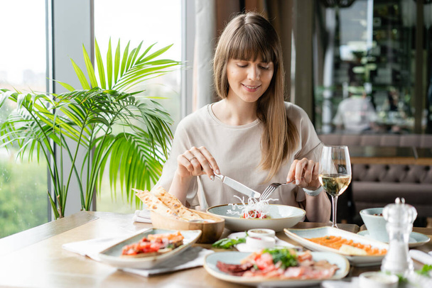 Retrato de una hermosa mujer joven y elegante en el restaurante con una copa de vino. Cena y una variedad de platos en la mesa. Cocina italiana
 - Foto, Imagen