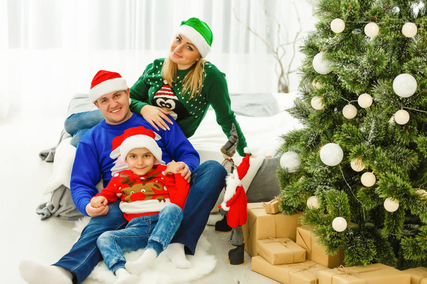 Viehättävä perhe istuu lähellä joulukuusi
 - Valokuva, kuva