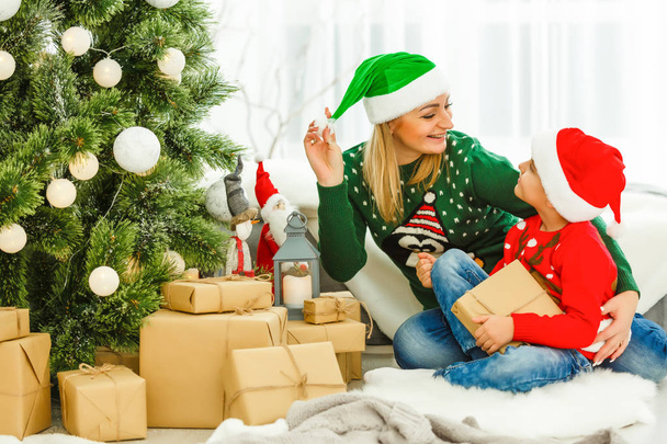 Young mother and her cute son sitting near Christmas tree with presents  - Fotoğraf, Görsel