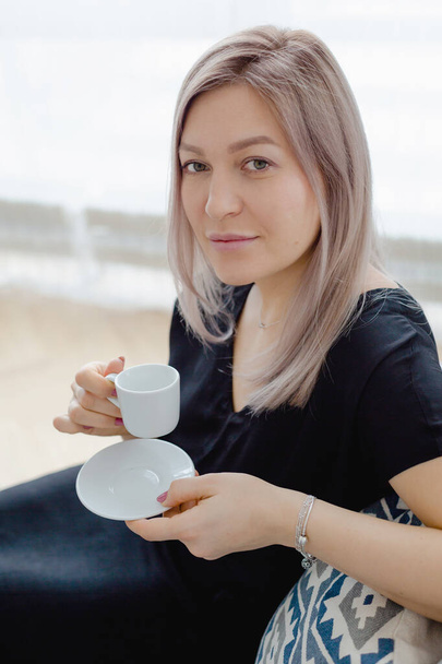 Blonde woman in a black dress drinks coffee - Foto, imagen