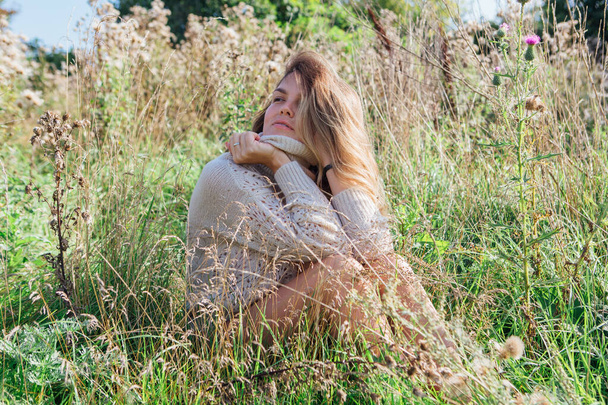 Happy young beautiful woman in sweater and underpants sitting with bare foot in a field of dry agrimony - Foto, Imagem