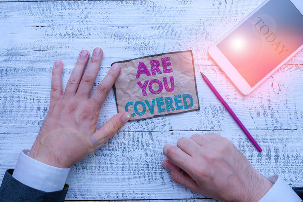 Text sign showing Are You Covered. Conceptual photo Asking about how medications are covered by your plan Hand hold note paper near writing equipment and modern smartphone device. - Photo, Image
