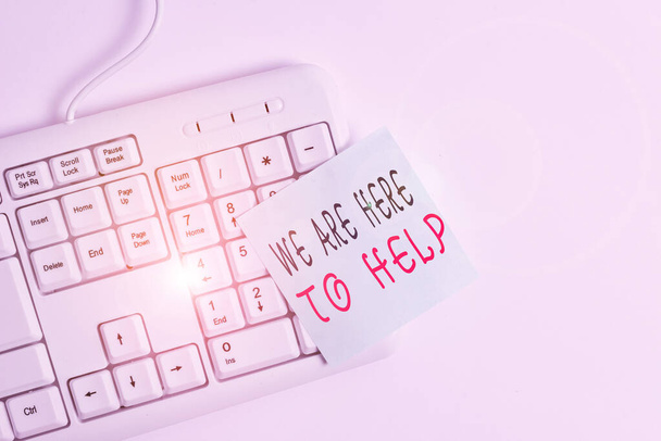 Writing note showing We Are Here To Help. Business photo showcasing Someone who is always ready to Assist Support Give White pc keyboard with empty note paper above white background. - Photo, Image