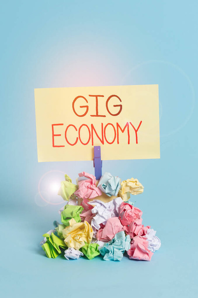 Pisanie tekstu Gig Economy. Koncepcja biznesowa dla systemu wolnego rynku, w którym tymczasowe pozycje są wspólne Przypomnienie stos pognieciony papier szpilka przypomnienie niebieski tło. - Zdjęcie, obraz