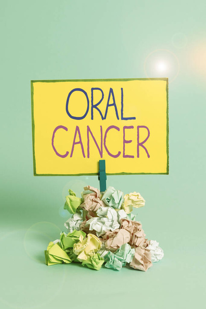 Text sign showing Oral Cancer. Conceptual photo the cancer of the lining of the lips mouth or upper throat Reminder pile colored crumpled paper clothespin reminder blue background. - Фото, изображение