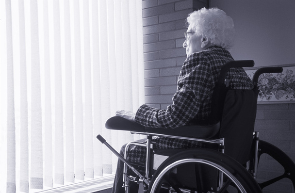 Senior Woman Sitting In Wheelchair Looking Out Of Window With Blinds - Zdjęcie, obraz