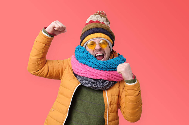 Young male in orange summer glasses and winter scarf clenches fists in joy, like a winner - Photo, Image