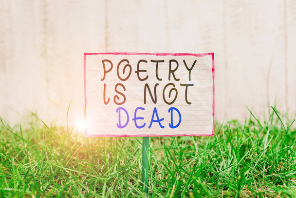 Znak tekstowy pokazujący, że Poezja nie umarła. Konceptualne zdjęcie estetyczne i rytmiczne pisanie jest wciąż żywy i nowoczesny pognieciony papier przymocowany do kija i umieszczony w zielonej trawiastej ziemi. - Zdjęcie, obraz