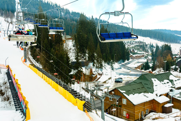 Wyciąg i stok narciarski z narciarzami pod nim w słoneczny zimowy dzień z błękitnym niebem, ośrodek narciarski Bukovel. - Zdjęcie, obraz