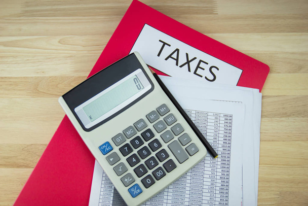 Documentos fiscales y archivos de papel, calculadora en el escritorio de madera en la oficina, concepto Pago anual de impuestos
 - Foto, Imagen