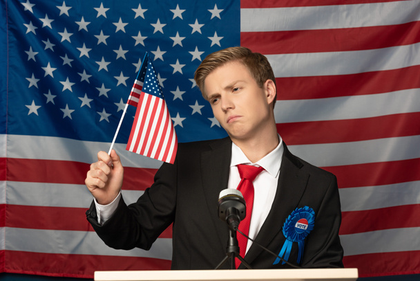 hombre disgustado en tribuna y portando bandera americana
 - Foto, Imagen