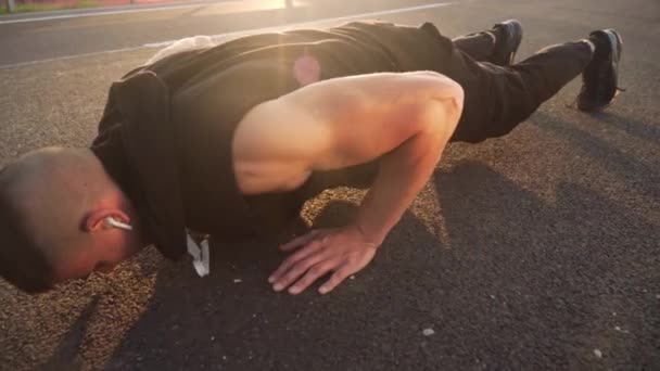 4k pan movement video of young fit man doing push ups in the morning outdoor on road in sunset with strong sun flare - Materiaali, video
