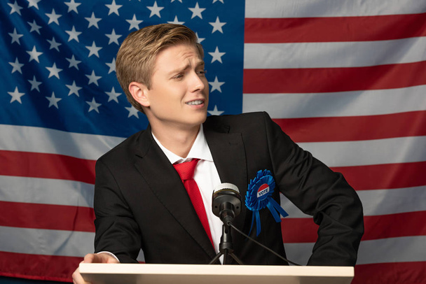 Selbstbewusster Mann auf der Tribüne vor dem Hintergrund der amerikanischen Flagge - Foto, Bild