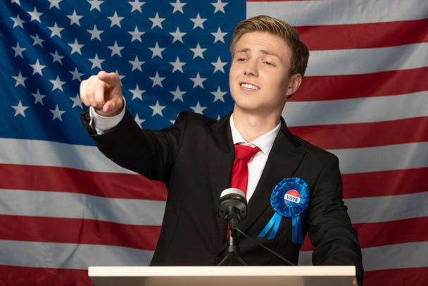 hombre confiado señalando con el dedo en tribuna sobre fondo de la bandera americana
 - Foto, Imagen