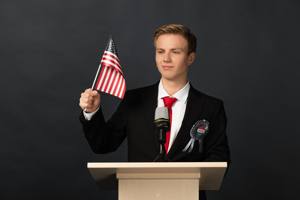 Lächelnder emotionaler Mann auf der Tribüne mit amerikanischer Flagge auf schwarzem Hintergrund - Foto, Bild